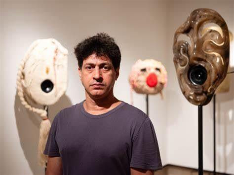 A photo of Yuval Avital standing in front of three sulptures