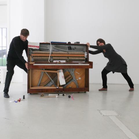 A photo of Dušica Cajlan and Georg Wissel pulling and pushing an upright piano